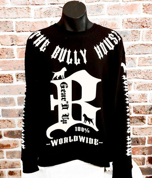 A black long sleeve jumper with white text and graphics, displayed on a mannequin against a brick wall.